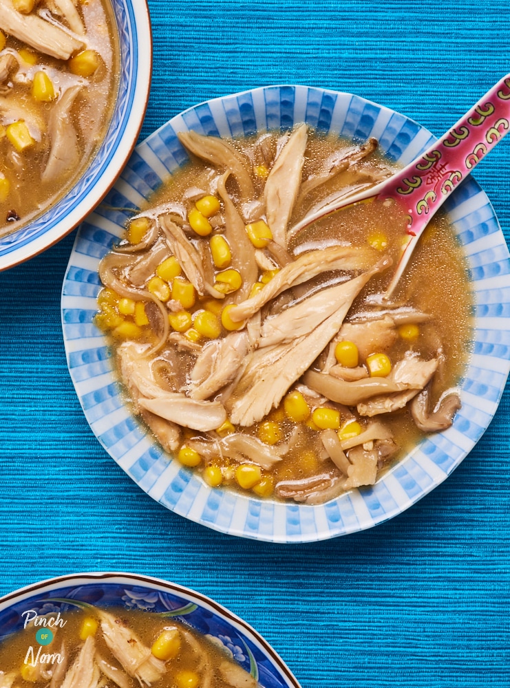 Three servings of Pinch of Nom's Chicken, Mushroom and Sweetcorn Soup are served in blue bowls, set on a bright blue surface. An Asian-style spoon rests in the central bowl.