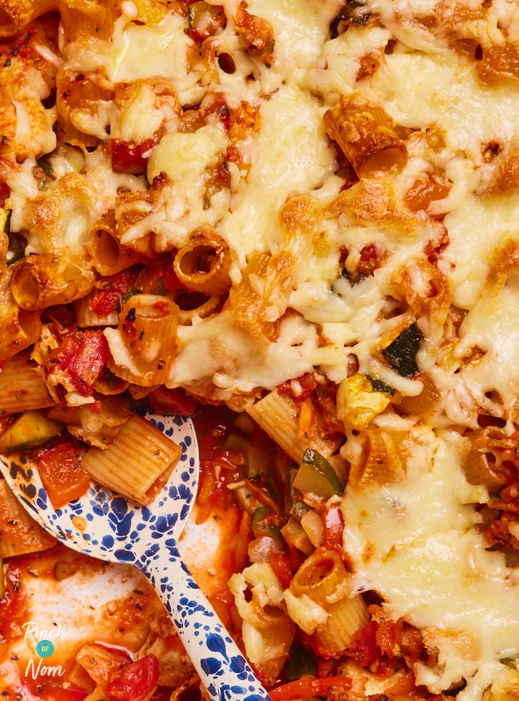 Pinch of Nom's slimming-friendly Turkey Ratatouille Pasta Bake is being dished out by a large spoon, showing the tomatoey centre and the gooey, cheesy topping.