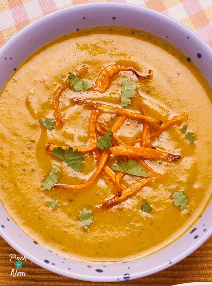 A bowl is filled with Pinch of Nom's slimming-friendly Carrot and Coriander Soup, topped with air-fried strips of carrot and a garnish of fresh coriander leaves.