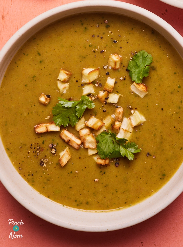 A bowl of Pinch of Nom's Curried Parsnip Soup is served on a bright tabletop; the soup is thick and creamy, topped with crispy parsnip chunks and freshly-chopped coriander leaves.