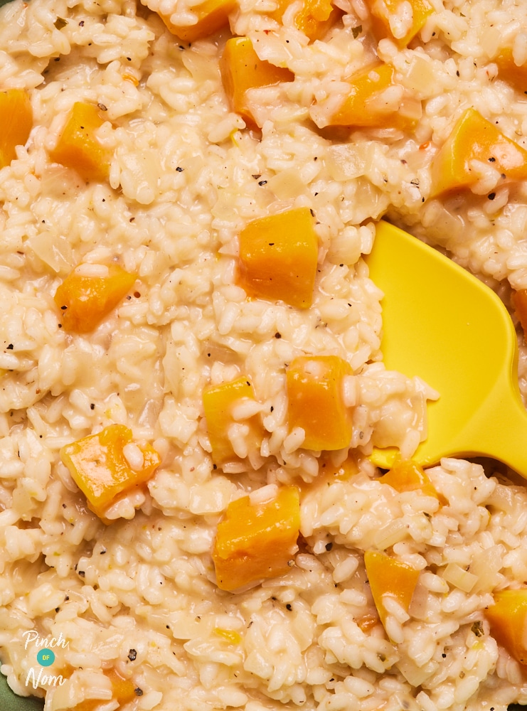 A close-up shows Pinch of Nom's Butternut Squash Risotto. The risotto is creamy, with chunks of orange butternut squash. A yellow serving spoon rests in the pan, ready to dish up.