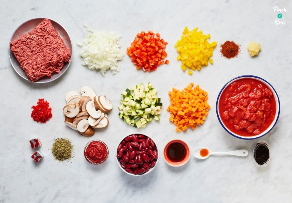 The raw ingredients for Pinch of Nom's Chilli Con Carne are laid out on a grey tabletop, chopped, portioned and ready to begin cooking.