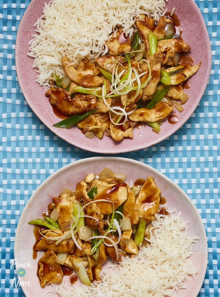 Two pink dinner plates are filled with Pinch of Nom's Chicken with Ginger and Spring Onion. The Chinese-style meal is served with fluffy white rice and garnished with shredded spring onions.