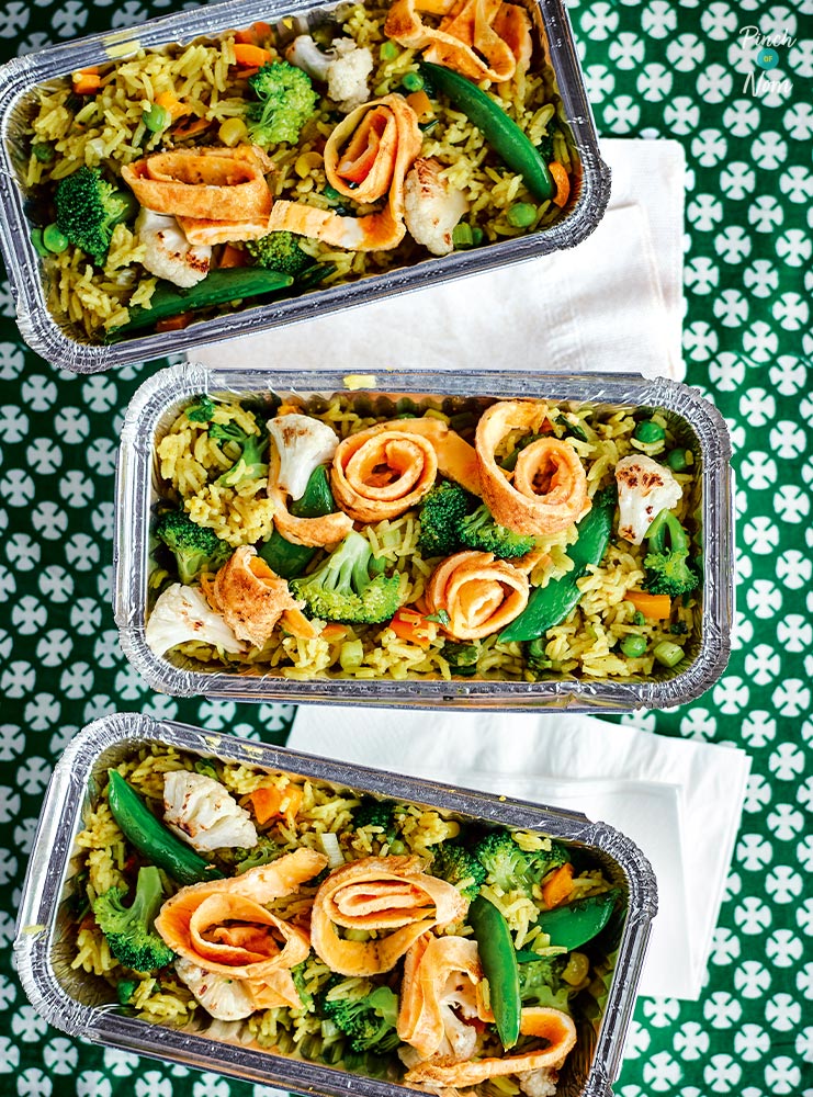 A table is set with takeaway-style trays filled with Pinch of Nom's Vegetable Biryani from the first cookbook.