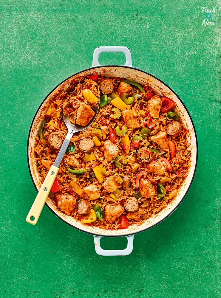 Pinch of Nom's Jambalaya is served in a large ovenproof casserole dish with a ladle waiting to dig in; it's bright and colourful, with lots of chopped sausages, peppers and rice.