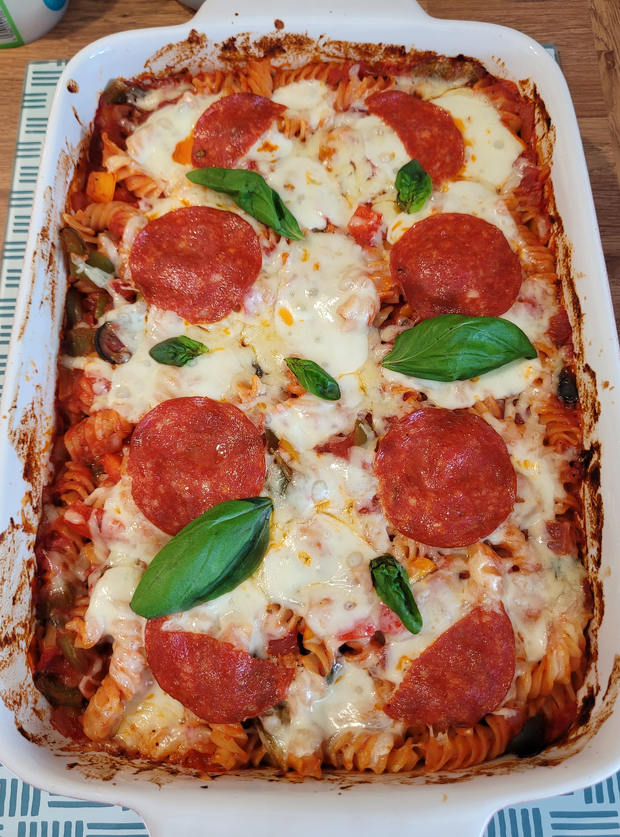 An image of Pinch of Nom's Pizza Pasta, uploaded to the Pinch of Nom website gallery by auntyellenskitchen. The recipe is served in an oven dish with freshly melted cheese on top, along with pepperoni pieces and basil leaves.