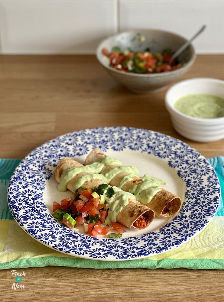 A portion of Pinch of Nom's Chipotle Chicken Taquitos from the Enjoy cookbook is served drizzled with creamy avocado sauce and a dollop of fresh homemade salsa.