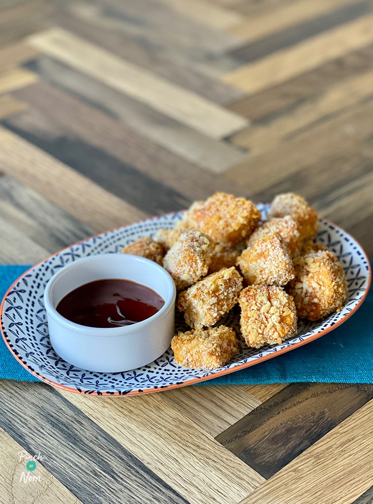 A plate of golden Crispy Tofu Nuggets from Pinch of Nom: Enjoy. The meat-free, vegan nuggets are served with a pot of spicy tomato dipping sauce.
