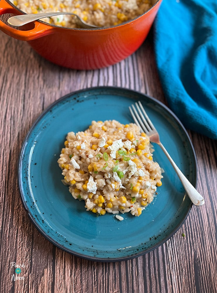 A table is set with a portion of Pinch of Nom's Sweetcorn Risotto, topped with a garnish of spring onions.