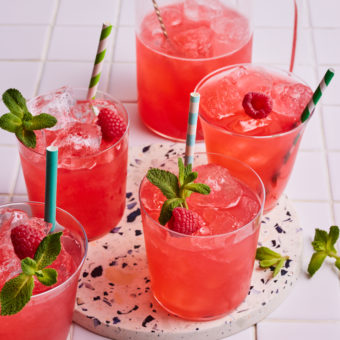 Pinch of Nom's Pink Lemonade is served in 4 glasses over ice with striped paper straws, fresh raspberries and a sprig of fresh mint.