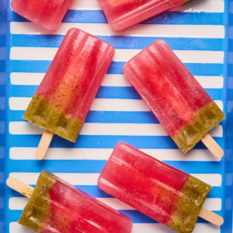 On a blue stripy background, 6 Strawberry and Kiwi Ice Lollies are laid out. They are juicy and red at the top, with a layer of green kiwi at the bottom.