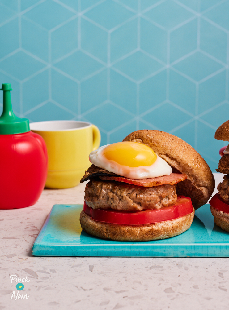 On a serving board, Pinch of Nom's slimming-friendly Breakfast Burgers are piled high, with a runny fried egg poking out from beneath the bun.