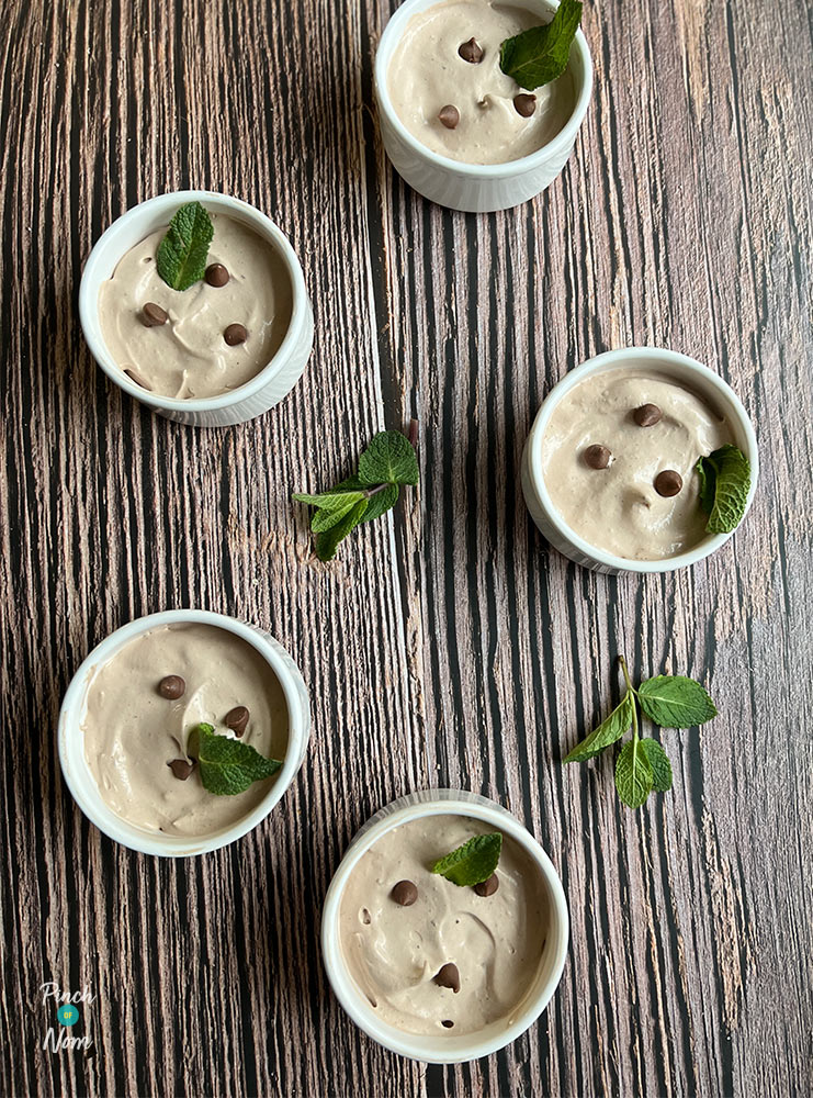 Five white ramekins are placed on a table, each one filled with Pinch of Nom's Mint Chocolate Mousse. The creamy mousse is topped with milk chocolate chips and decorated with fresh sprigs of mint.