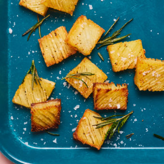 A tray of golden brown Accordion Potatoes. The rectangular potatoes are crispy at the edges, sprinkled with sea salt and fresh herbs.