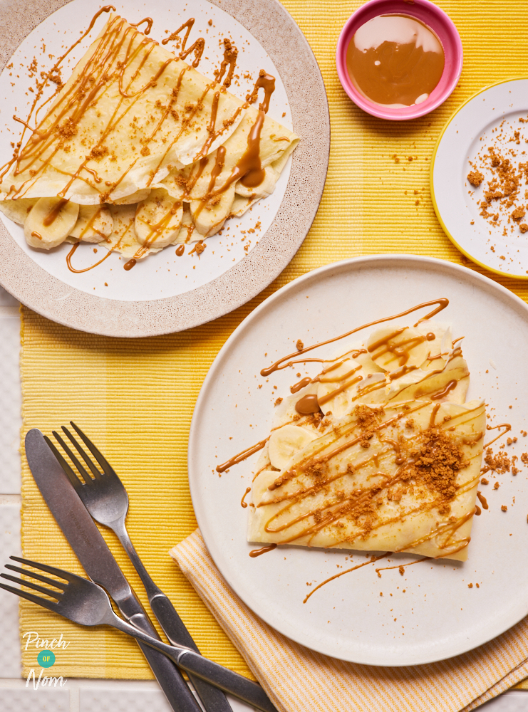 Two of Pinch of Nom's Banana and Biscoff Pancakes served on plates on a yellow tabletop with extra smooth Biscoff spread in a small bowl for dipping.