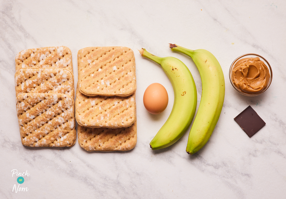 The ingredients for Pinch of Noms' easy Banana Biscoff Bakes recipe are laid out. There are 6 sandwich thins, two bananas, an egg, a square of chocolate and a small pot of Biscoff spread.
