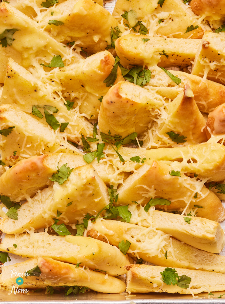 A close-up of Pinch of Nom's Cheesy Garlic Naan; the triangles have been baked until golden brown, topped with melty cheese and sprinkled with chopped coriander.