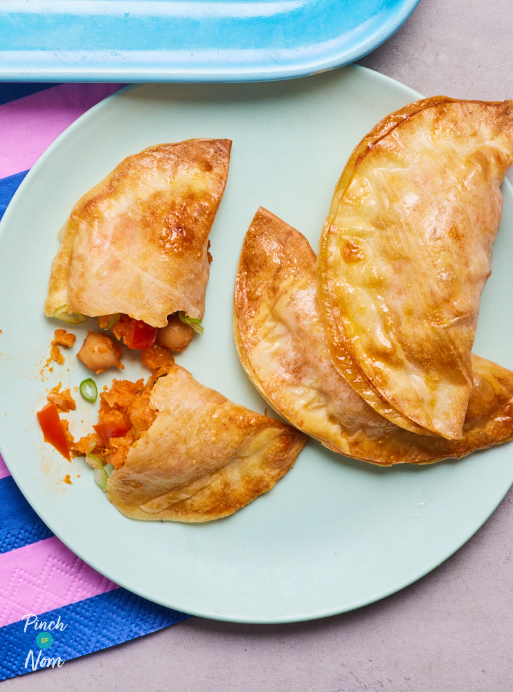 Three Empanadas are served on a pale green plate. One has been cut in half to reveal the vegetable filling inside the golden pastry.