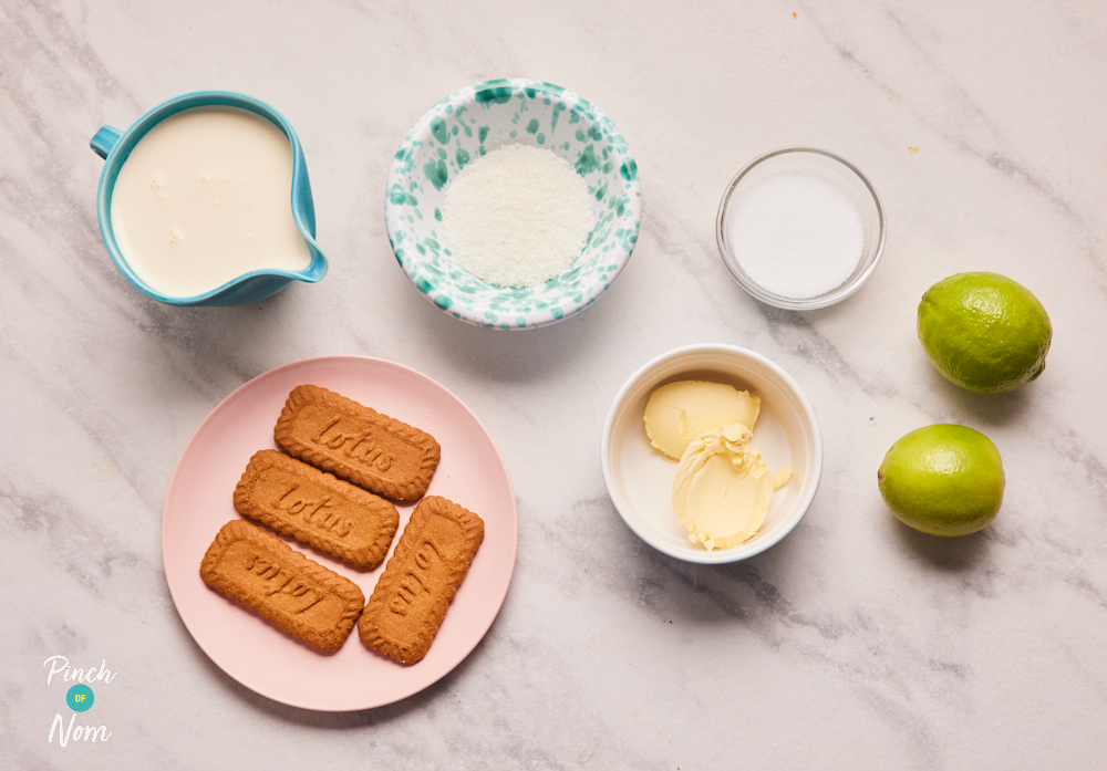 The ingredients for Pinch of Nom's Creamy Lime and Coconut Pots are laid out on a kitchen counter. There's light double cream alternative, limes, sweetener, redued-fat spread, desiccated coconut and Lotus Biscoff biscuits.
