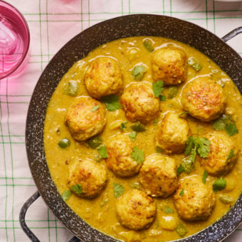Pinch of Nom's healthy family-friendly Korma Meatballs are served in a wide, deep pan. The golden meatballs sit in a rich, creamy, korma-style sauce, sprinkled with chopped coriander.