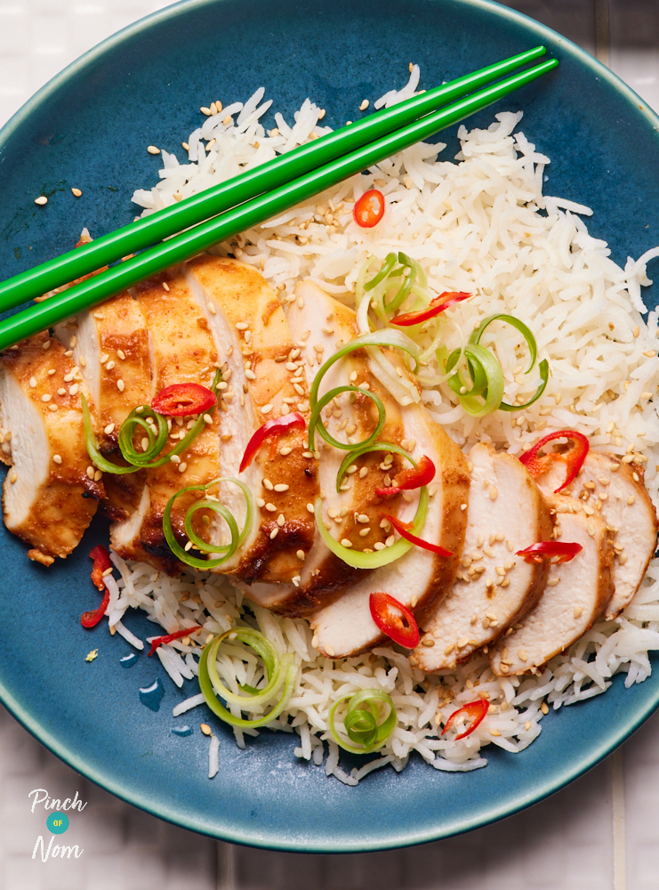 The cooked Miso Chilli Chicken has been sliced and served on top of a bed of fluffy jasmine rice. Finely sliced chillies and spring onions are sprinkled over the top, and a pair of green chopsticks are balanced on the plate, ready to dig in.
