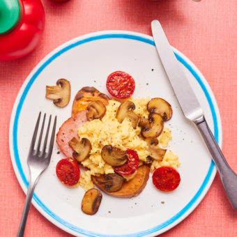 Pinch of Nom's Sweet Potato Breakfast Toast is served topped with eggs, mushrooms, bacon and tomatoes with cutlery waiting to dig in alongside ketchup for squeezing on top.