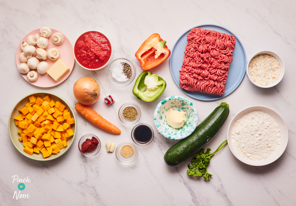 The ingredients for Pinch of Nom's Beef Crumble are laid out on a kitchen counter. The beef mince and vegetables are ready to be chopped, with the herbs and seasonings measured into small bowls.