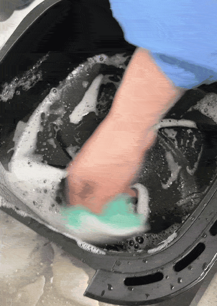 An air fryer basket is being scrubbed with a sponge and a soapy water.