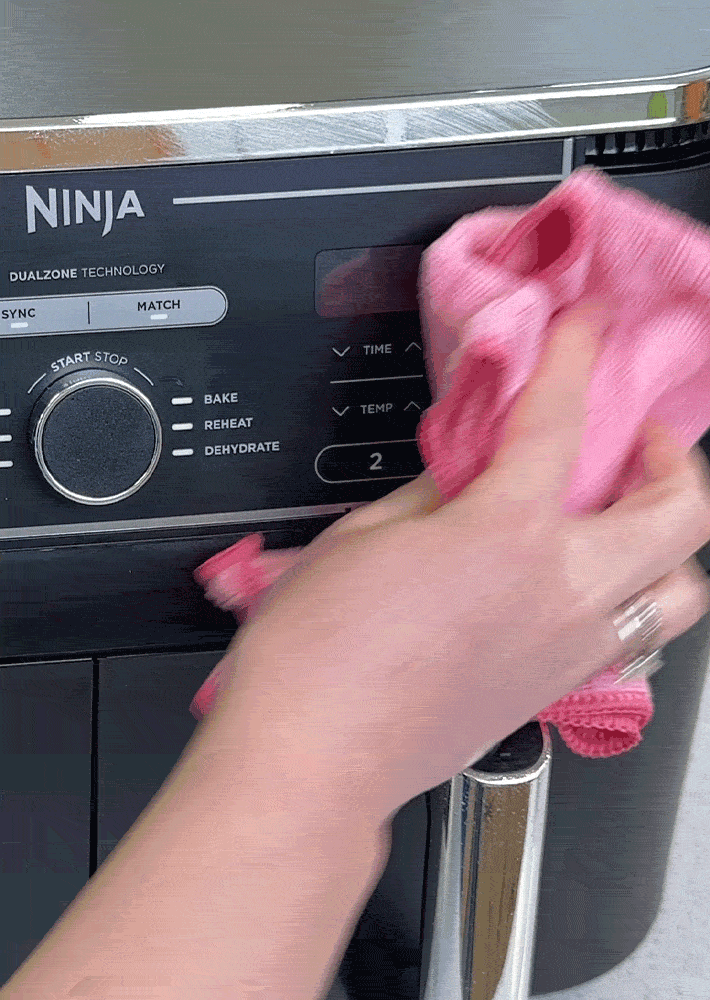An air fryer is being wiped on the outside with a microfibre cloth.