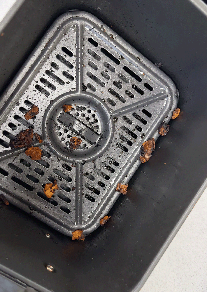 An air fryer basket with bits of grease and grime clinging to the bottom and sides.