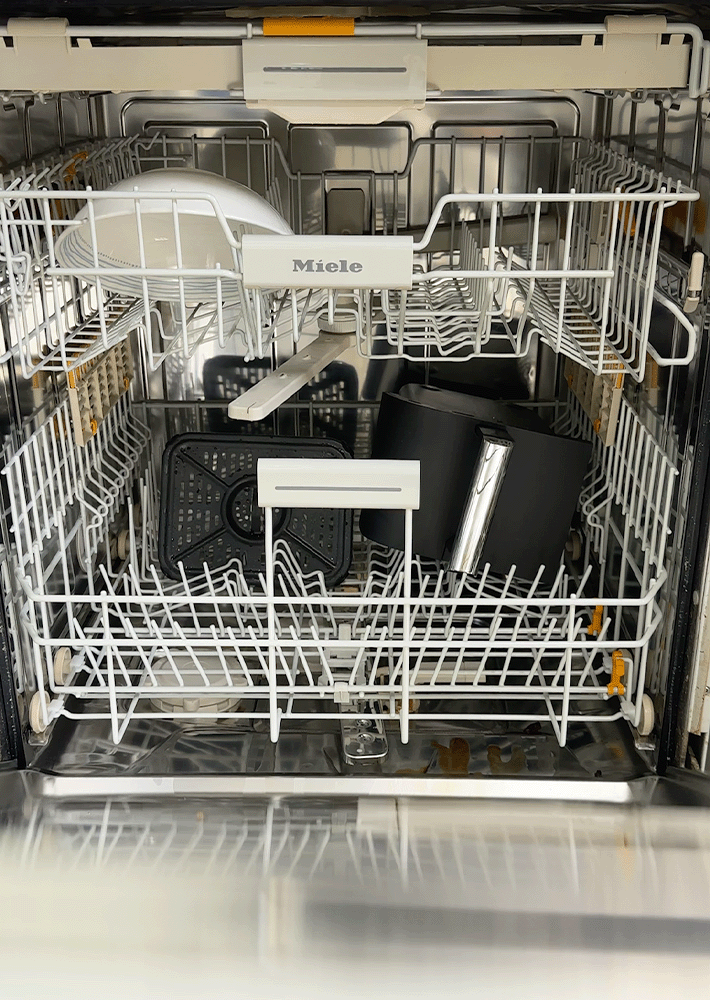 A dishwasher is loaded with dishwasher-safe air fryer parts, including trays, baskets and drawers.