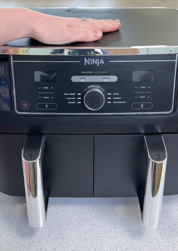 A hand rests proudly on a freshly-cleaned, sparkling-like-new Ninja air fryer unit with dual drawers. 