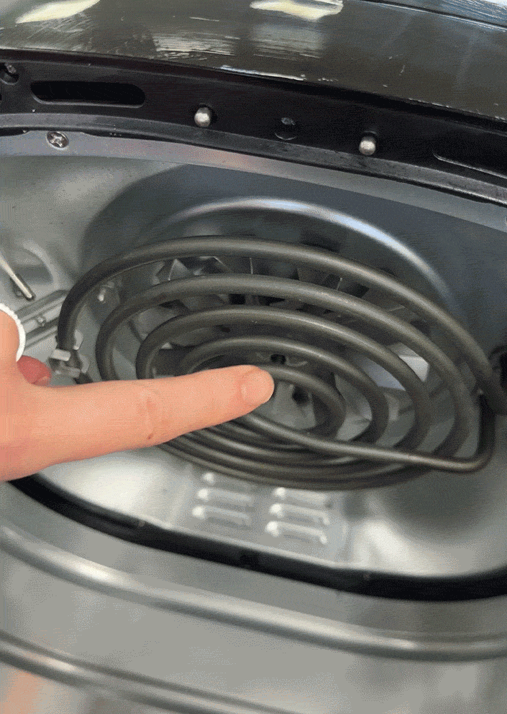 A finger is pointing out the heating element on the inside inner lid of an air fryer main unit.