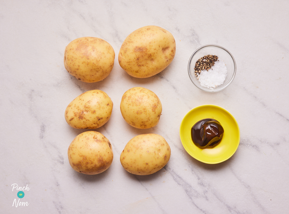 The ingredients for Pinch of Nom's Marmite Mash are laid out on a kitchen counter. The potatoes are ready to be chopped, with the Marmite and salt and pepper measured into small bowls.