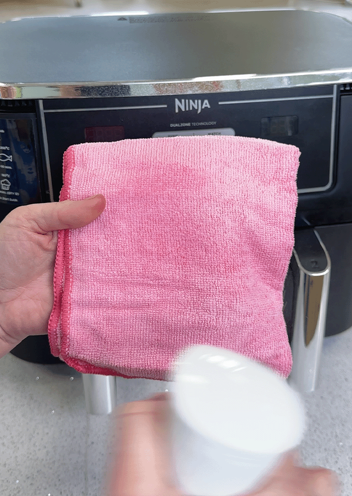 A microfibre cloth sprayed with all-purpose cleaner ready to wipe an air fryer clean.