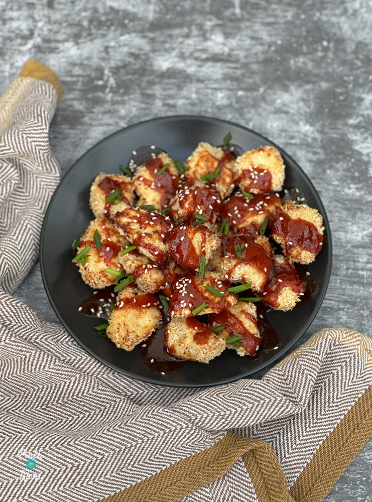 A bowl is filled with Pinch of Nom's Air Fryer Gochujang Chicken Nuggets from the Air Fryer cookbook; the nuggets are covered with homemade sauce and topped with chopped chives.