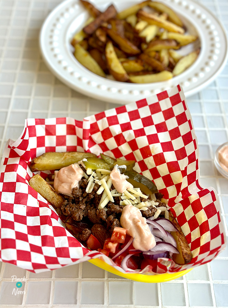 An American diner-style basket is served with Pinch of Nom's Air Fryer Loaded Cheeseburger Fries inside from the Air Fryer cookbook; topped with gherkins, burger-style sauce, onions and mince.