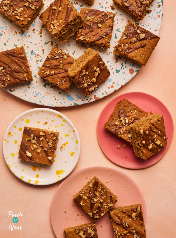 Pinch of Nom's Coffee and Walnut Sponge Traybake is sliced into 16 individual squares, ready to be shared onto 3 separate plates. Each slice is topped with a drizzle of coffee icing and a sprinkling of chopped walnuts.