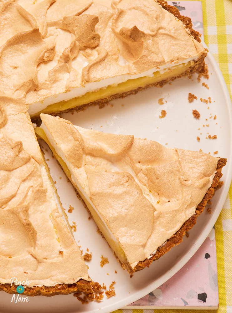 A close up photo shows a slice of Lemon Meringue Pie, ready to be served. The biscuit case is crisp and golden, and the layers of lemon filling and fluffy meringue can be seen.