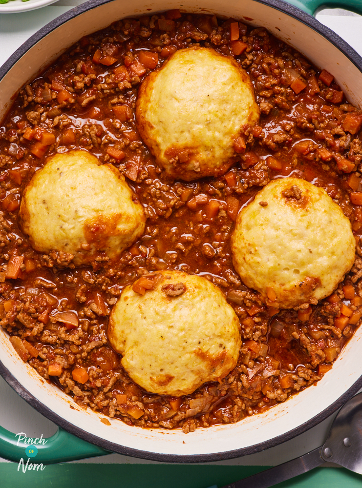 A close-up of Pinch of Nom's Mince and Dumplings served in a large, colourful casserole dish topped with puffed-up golden dumplings on a thick and rich bed of minced meat and vegetables.