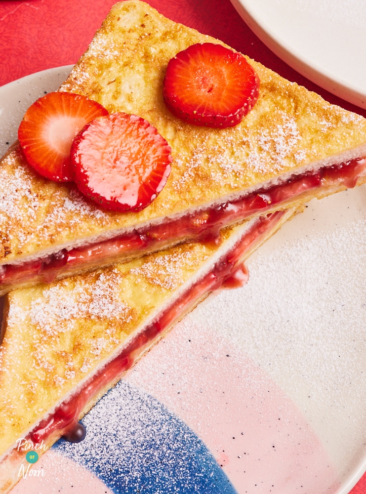 A close up of the Peanut Butter and Jelly French Toast shows the golden bread with its strawberry and peanut filling. The French toast is cut into 2 triangles, dusted with icing sugar and slices of strawberry have been stacked on top.