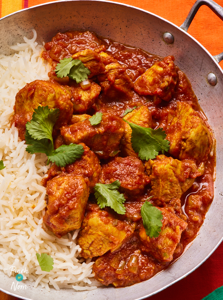 A close up shows Pinch of Nom's Chicken Madras, served in a large, shallow silver pan with fluffy white basmati rice. Fresh coriander has been sprinkled on the top.