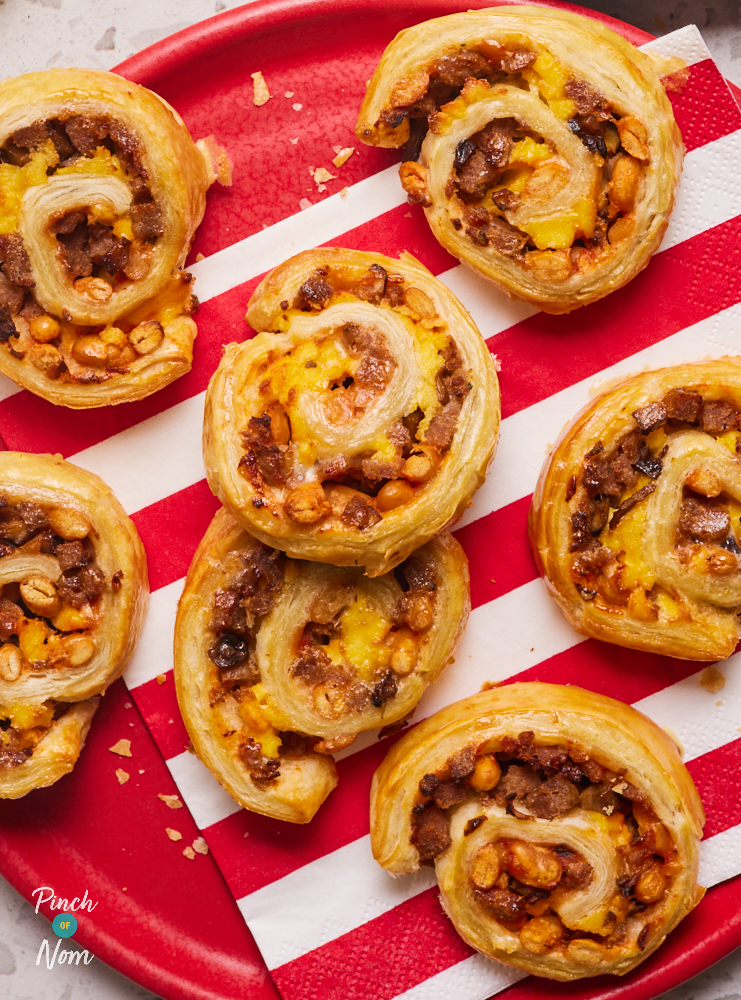On a red plate, several Full English Pinwheels are served, on top of a red and white striped napkin. The pastry swirls are golden brown, and the breakfast-themed filling can be seen running through the middle.