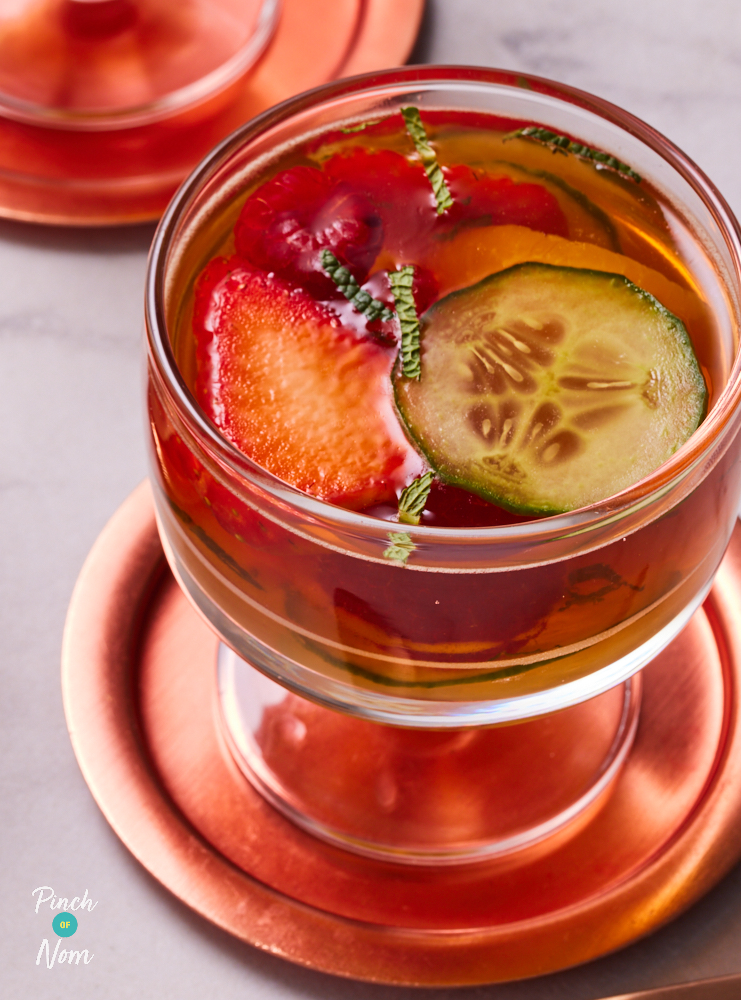 A close-up of Pinch of Nom's Pimms Jelly recipe served in a glass with an assortment of fruits poking out in the middle.