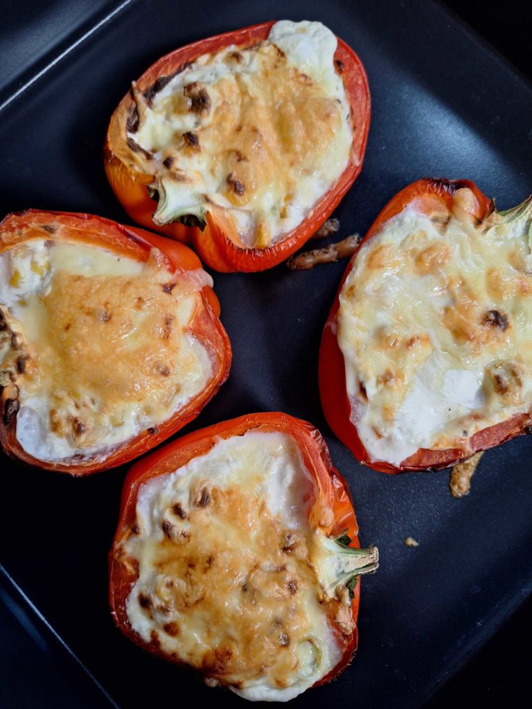 A tray is laid with Pinch of Nom's Cheese, Onion and Sweetcorn-Stuffed Peppers from the Air Fryer cookbook; the melty, cheesy centres are golden brown on top.