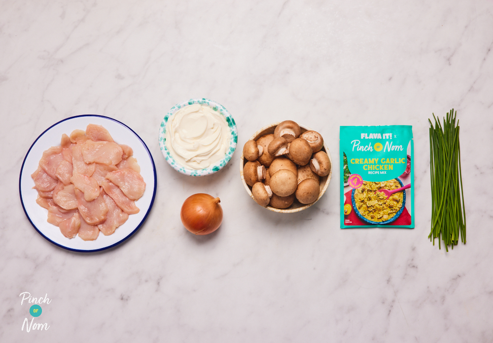 The ingredients for Pinch of Nom X Flava It! Creamy Garlic Chicken are laid out on a kitchen surface. The recipe mix seasoning sachet is set out beside chicken, cream cheese, mushrooms and an onion.