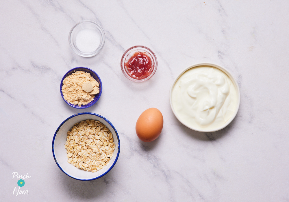 The ingredients for Pinch of Nom's Peanut Butter and Jelly Baked Oats recipe are laid out on a kitchen worktop. The ingredients are measured out into individual bowls, ready to start cooking.