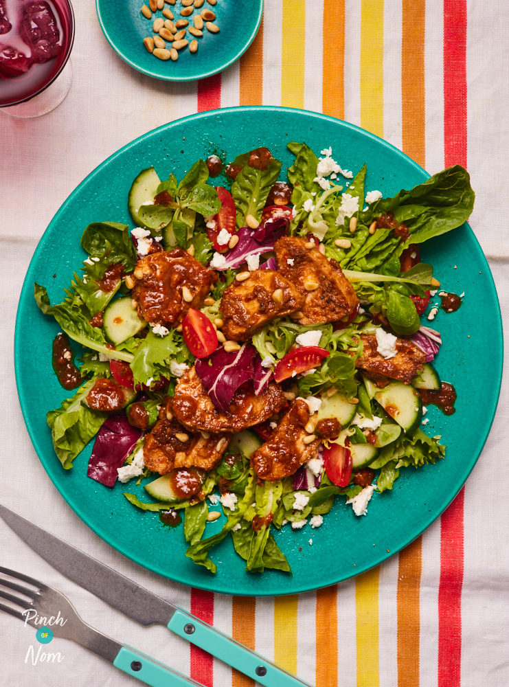 Pinch of Nom's Red Pesto Chicken Salad is served on a vibrant green plate. The table is laid with a colourful striped tablecloth and matching colourful cutlery.