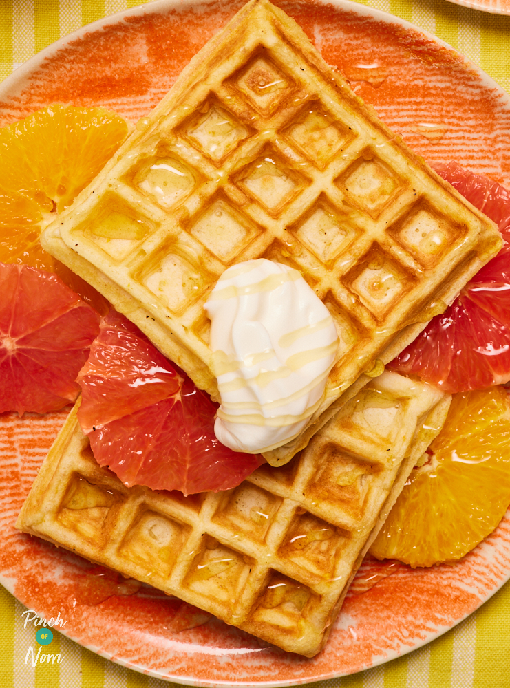 A close-up image of Pinch of Nom's Sunshine Waffles, topped with juicy-looking fruit segments and a dollop of yoghurt.