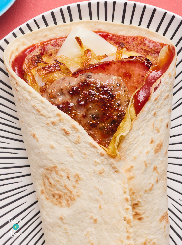 A close-up of Pinch of Nom's Breakfast Wrap served on a funky plate filled with sausage, bacon, cheese, egg and ketchup.